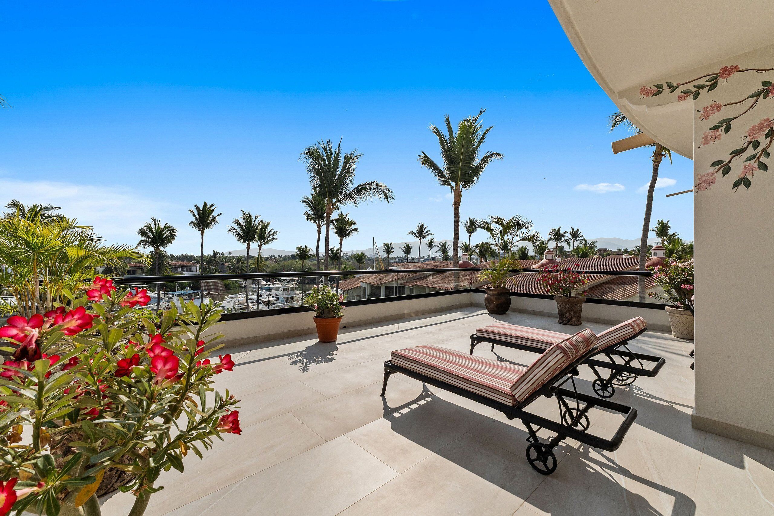 A balcony with lounge chairs, potted plants, and a view of palm trees and buildings.