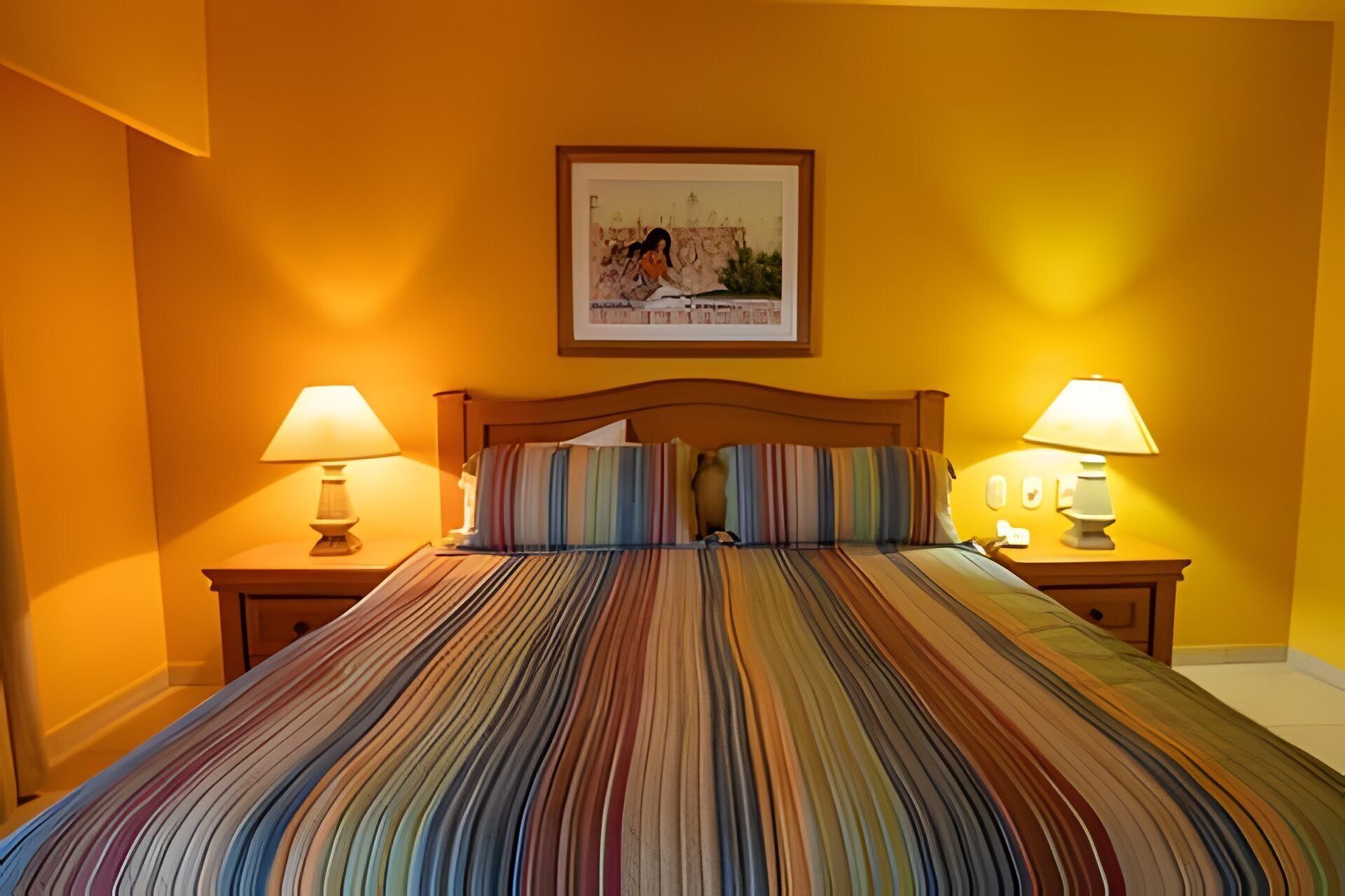 A bed with a striped bedspread, two bedside lamps, and a framed picture on the wall.