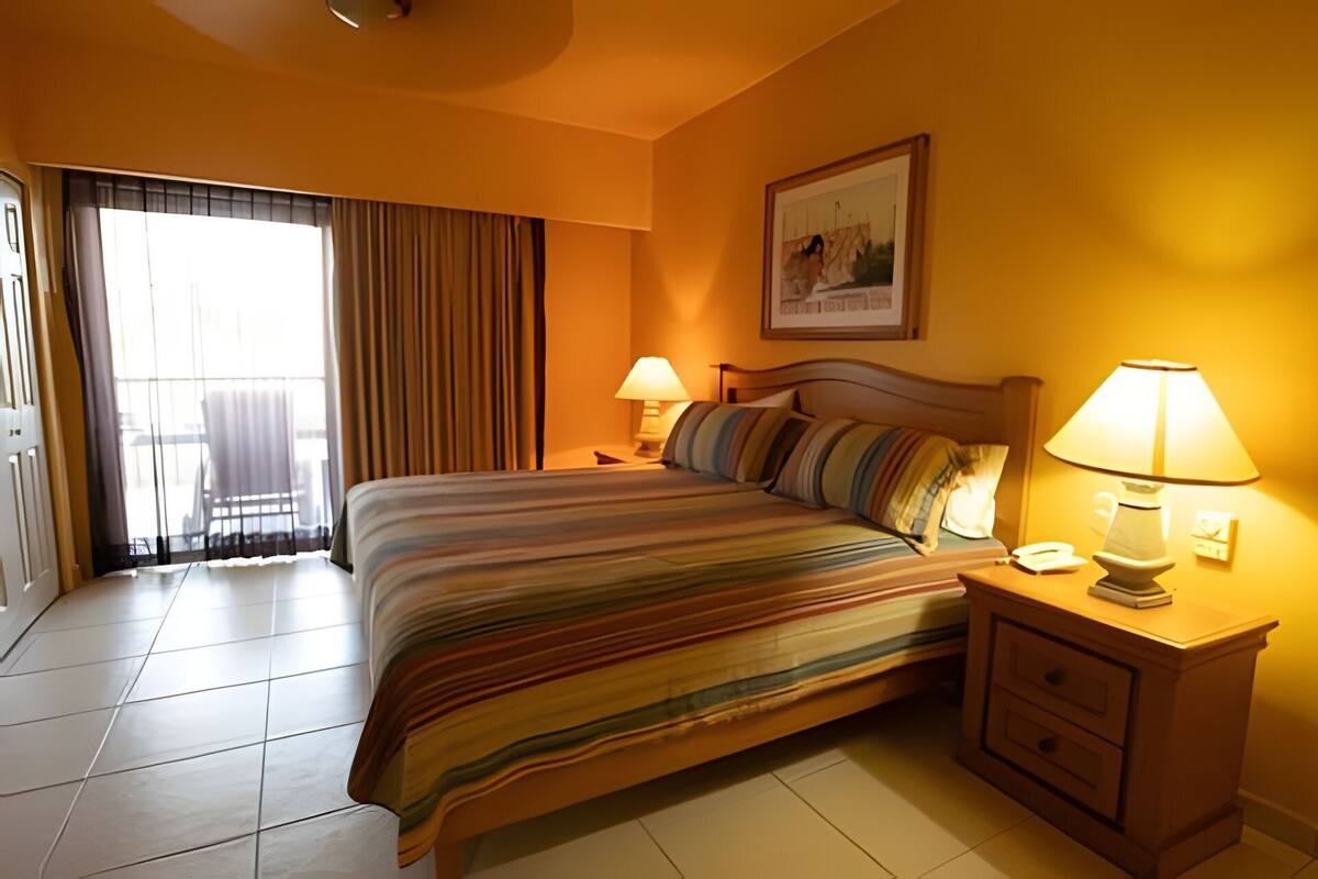 A hotel room with a large bed, two bedside lamps, a nightstand, a framed picture on the wall, and a window with curtains.