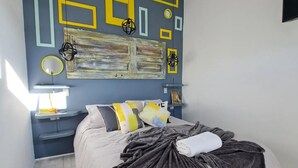 Une chambre moderne avec un lit, des tables de chevet et un mur orné d’œuvres d’art aux motifs géométriques.