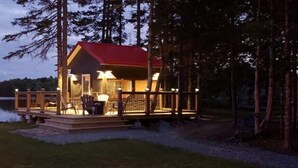 Una cabaña con techo rojo, una terraza con sillas y vista a un lago.