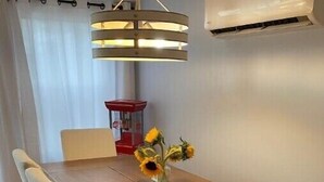 Una mesa de comedor con cuatro sillas, un jarrón con girasoles, una lámpara colgante y un objeto rojo al fondo.
