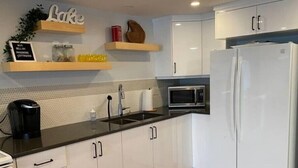Una cocina moderna con armarios blancos, encimera negra, refrigerador blanco, microondas y cafetera.