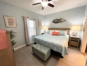 A bedroom with a bed, a nightstand, a ceiling fan, and a window with curtains.