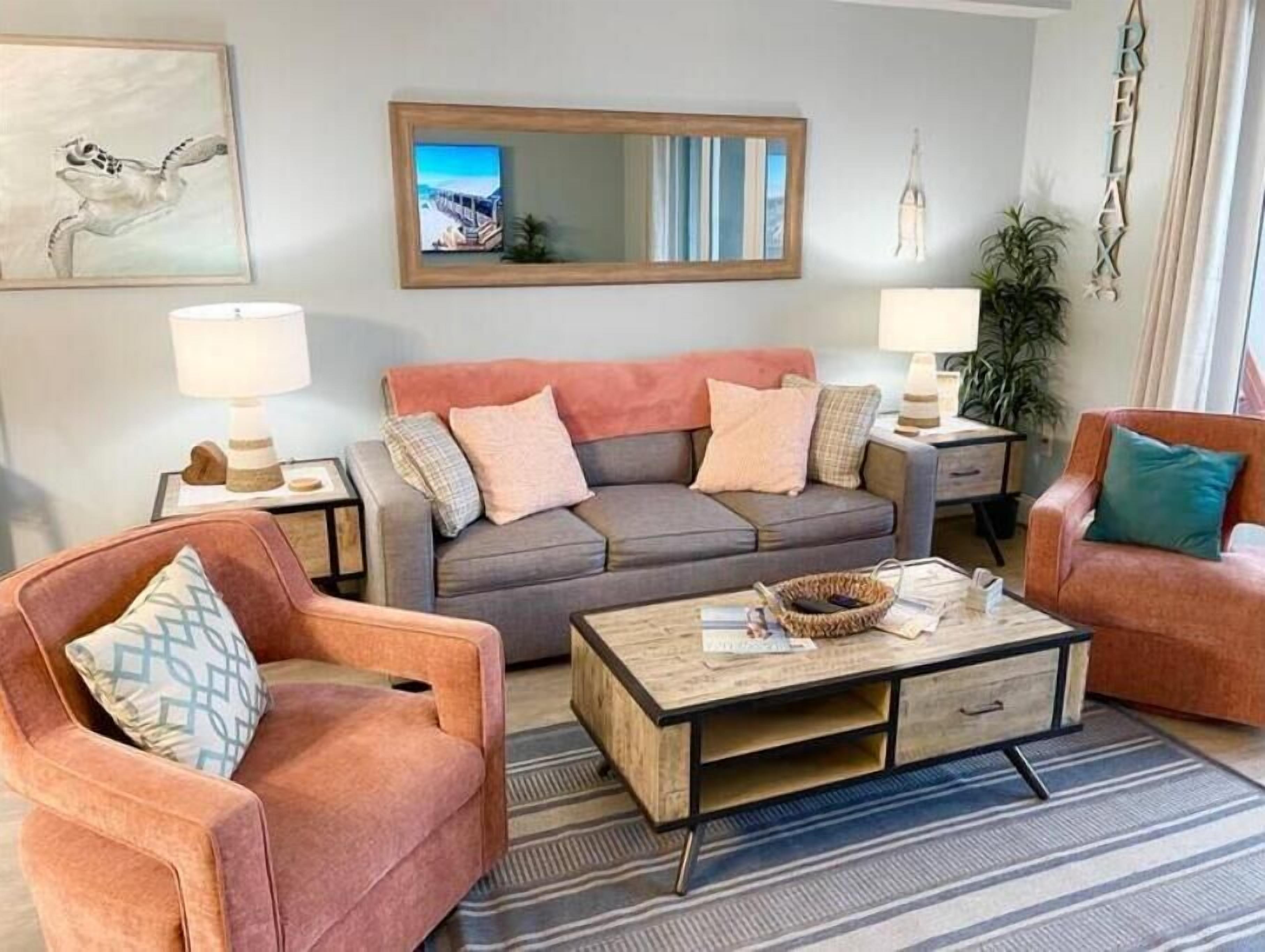A living room with a grey sofa, two armchairs, a coffee table, and a large mirror.