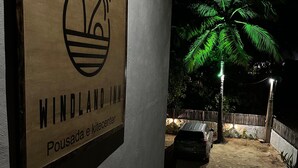 Μια ξύλινη πινακίδα με το λογότυπο ενός φοίνικα και την επιγραφή «Windland Inn», που υποδηλώνει μια άνετη τοποθεσία, ενδεχομένως δίπλα στην παραλία.