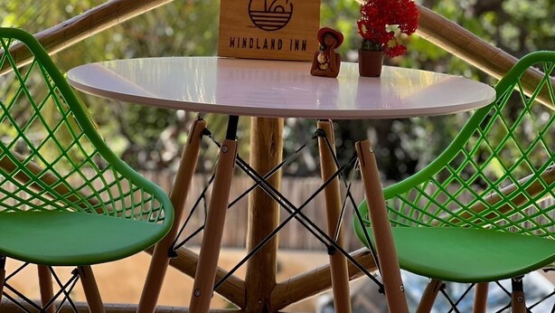 Μια ξύλινη πινακίδα με την επιγραφή «Windland Inn», ένα μικρό τραπέζι με μια γλάστρα και δύο πράσινες καρέκλες.