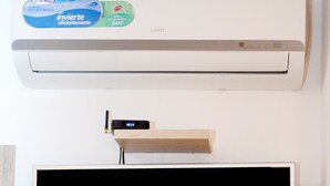 Un climatiseur fixé au mur, orné d’un autocollant indiquant son niveau d’efficacité énergétique. En dessous, un téléviseur à écran plat affiche le mot « NETFLIX » en lettres rouges.