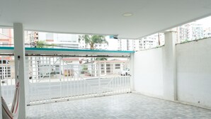 Une pièce vide avec un sol carrelé, un mur blanc et une vue sur un espace clos, avec des bâtiments et une rue.