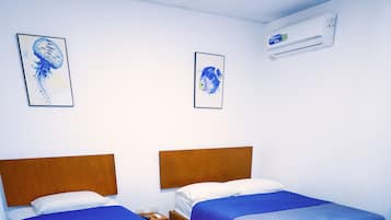 A hotel room with two beds, wooden headboards, and blue bedding. There are two framed pictures on the wall.