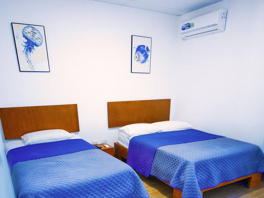 A hotel room with two beds, wooden headboards, and blue bedding. There are two framed pictures on the wall.