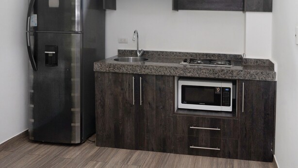 Une cuisine moderne avec des meubles de couleur bois foncé, un réfrigérateur en acier inoxydable, un four à micro-ondes encastré et une cuisinière à gaz.
