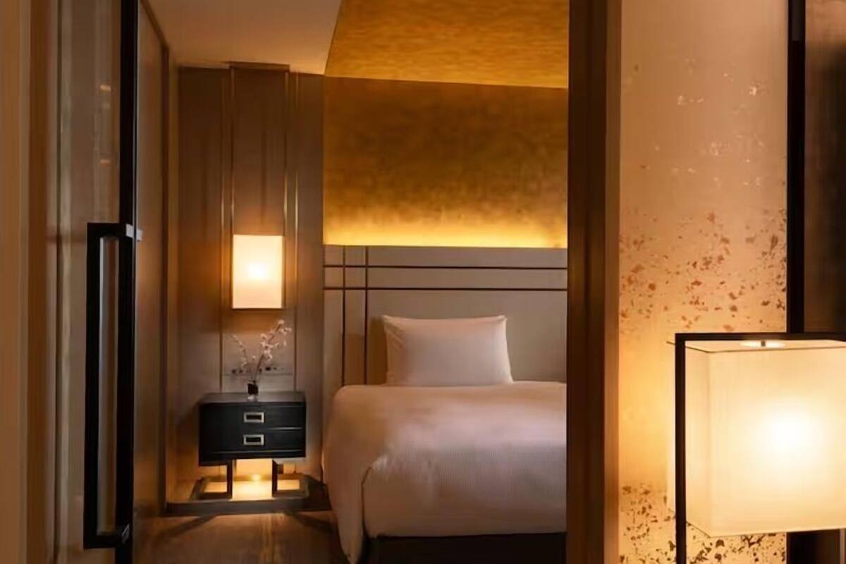 A hotel room with a bed, bedside table, lamp, and a wall with a textured pattern.