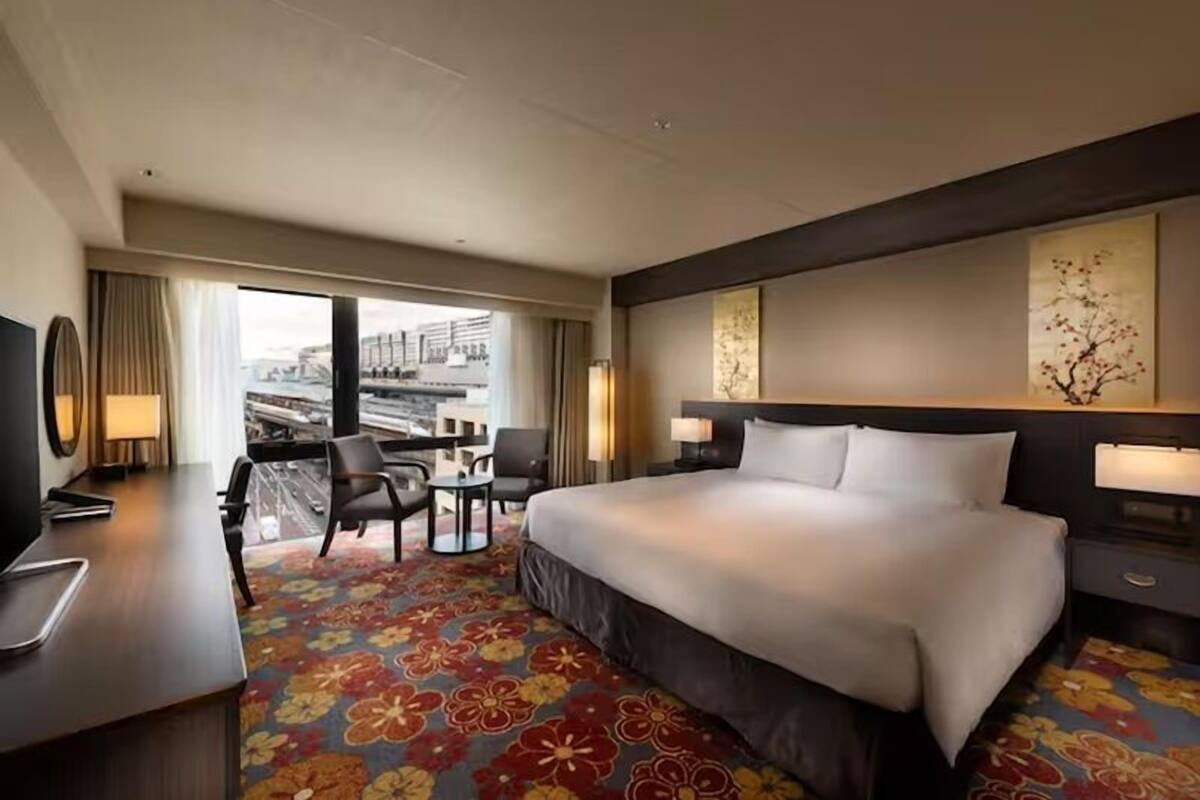 A hotel room with a large bed, a desk with a chair, a small table, and a TV.