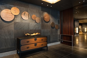 Un hall d’entrée moderne avec un sol carrelé foncé, une console en bois dotée de tiroirs et une série d’œuvres d’art murales en bois de forme circulaire.