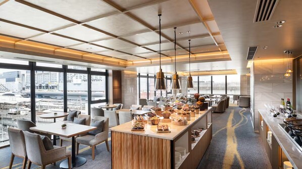Un moderno vestíbulo de hotel con una zona de bar central, espacios de asiento y grandes ventanales con vistas a la ciudad.