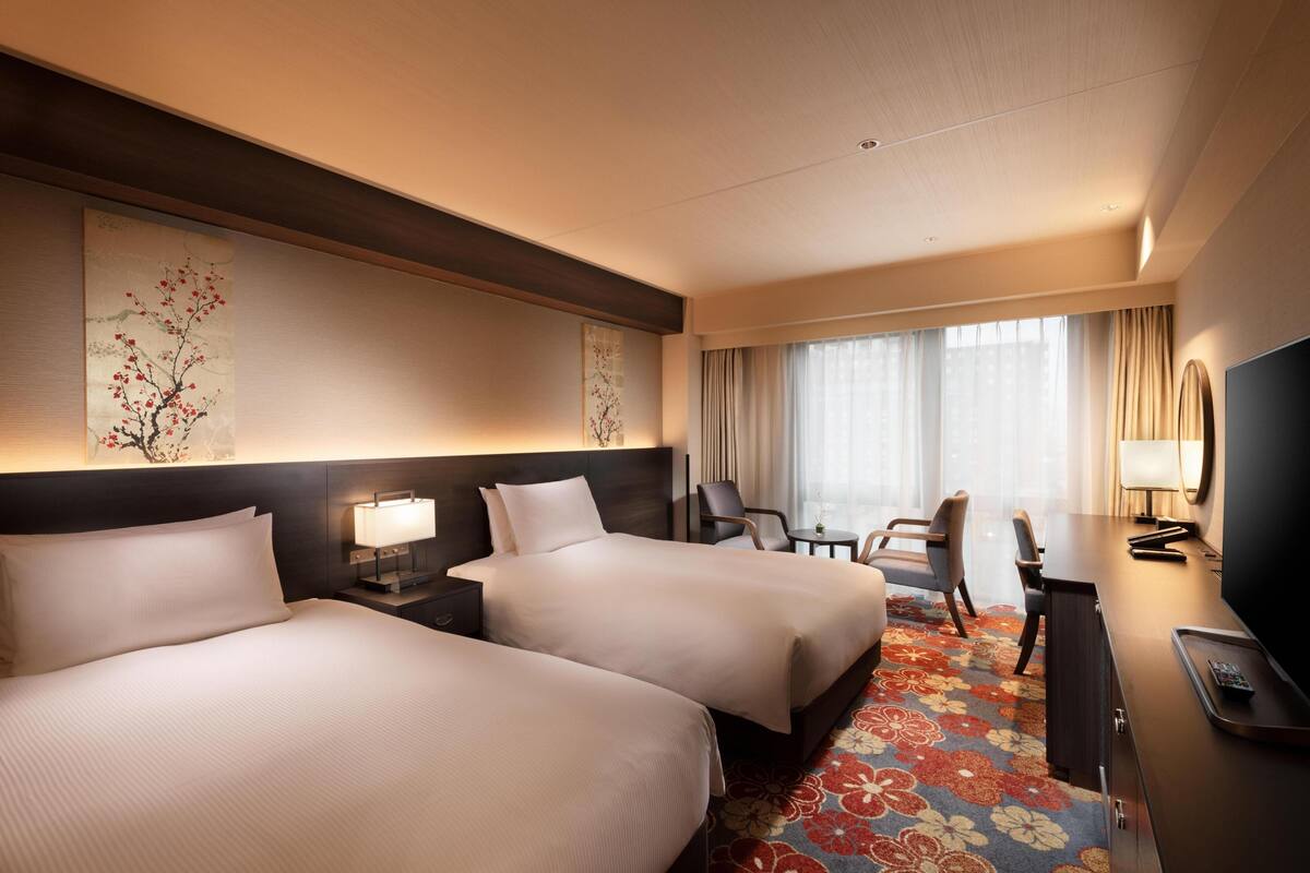 A hotel room with two beds, a desk, a TV, and a window with curtains.
