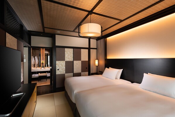 Quarto de hotel com cama, televisão, escrivaninha e banheiro visível por uma porta aberta.