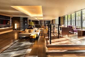 Un hall d'hotel modern amb zona d'estar, taulell de recepció i grans finestres amb vista a l'exterior.