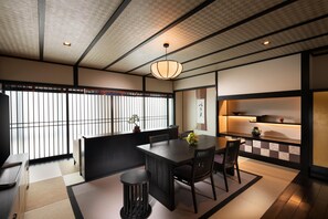 Een traditionele Japanse kamer met tatami vloeren, een lage tafel met stoelen, een schuifdeur en een plankje met decoratieve objecten.
