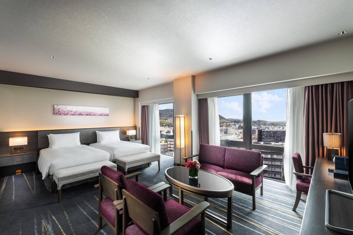 A hotel room with two beds, a sofa, a coffee table, and a desk with a lamp.