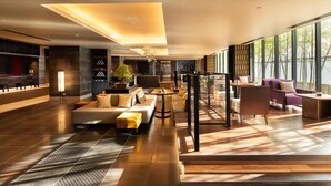 En moderne hotellobby med et siddeområde, en reception og store vinduer med udsigt udendørs.