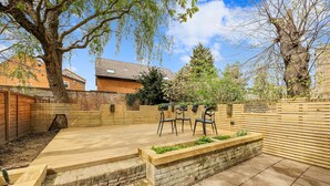 Une terrasse avec un sol en béton, des marches en bois et un bac à fleurs surélevé où sont plantées des plantes.
