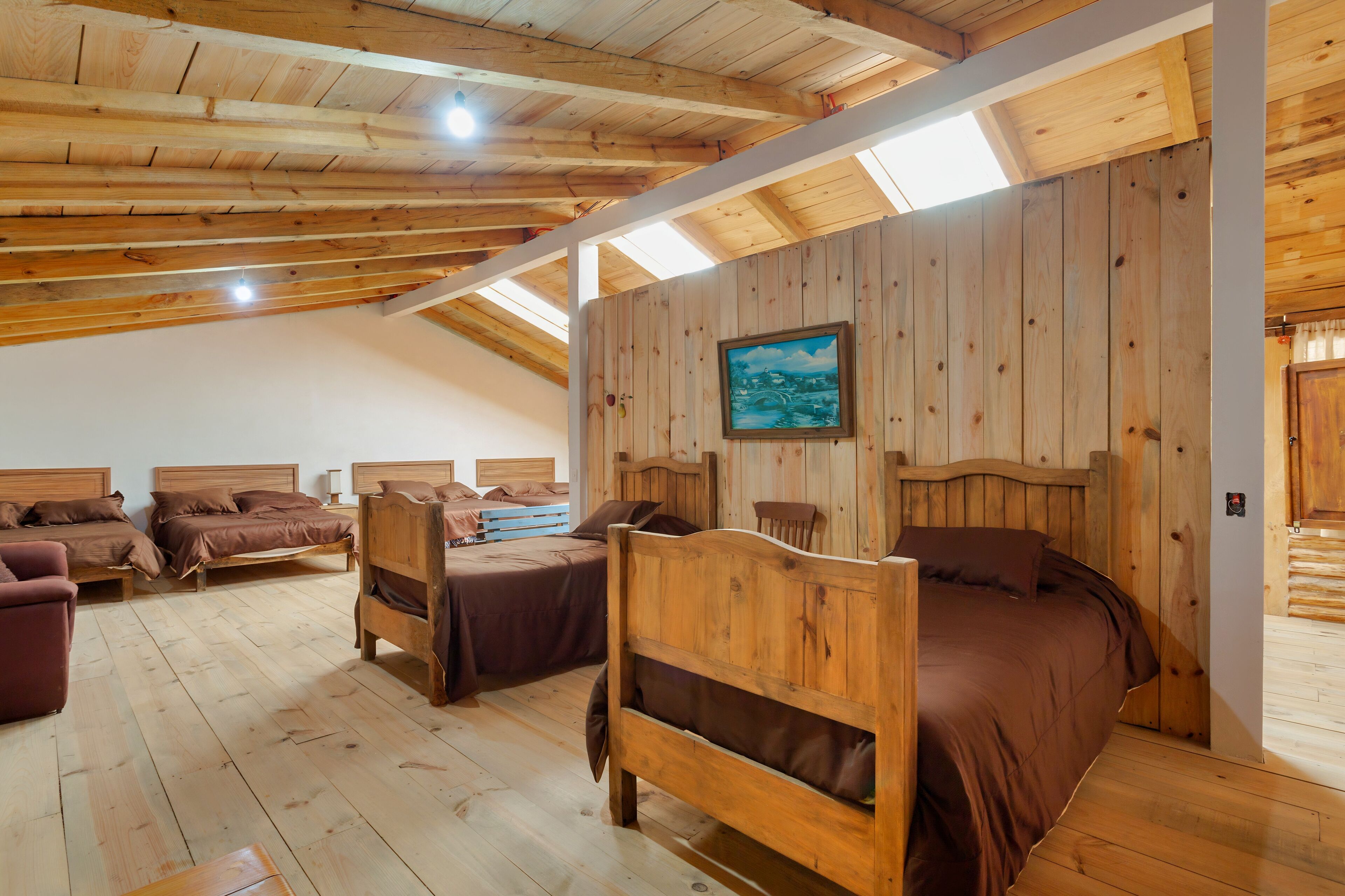A wooden interior with four beds, a sofa, and a painting on the wall.