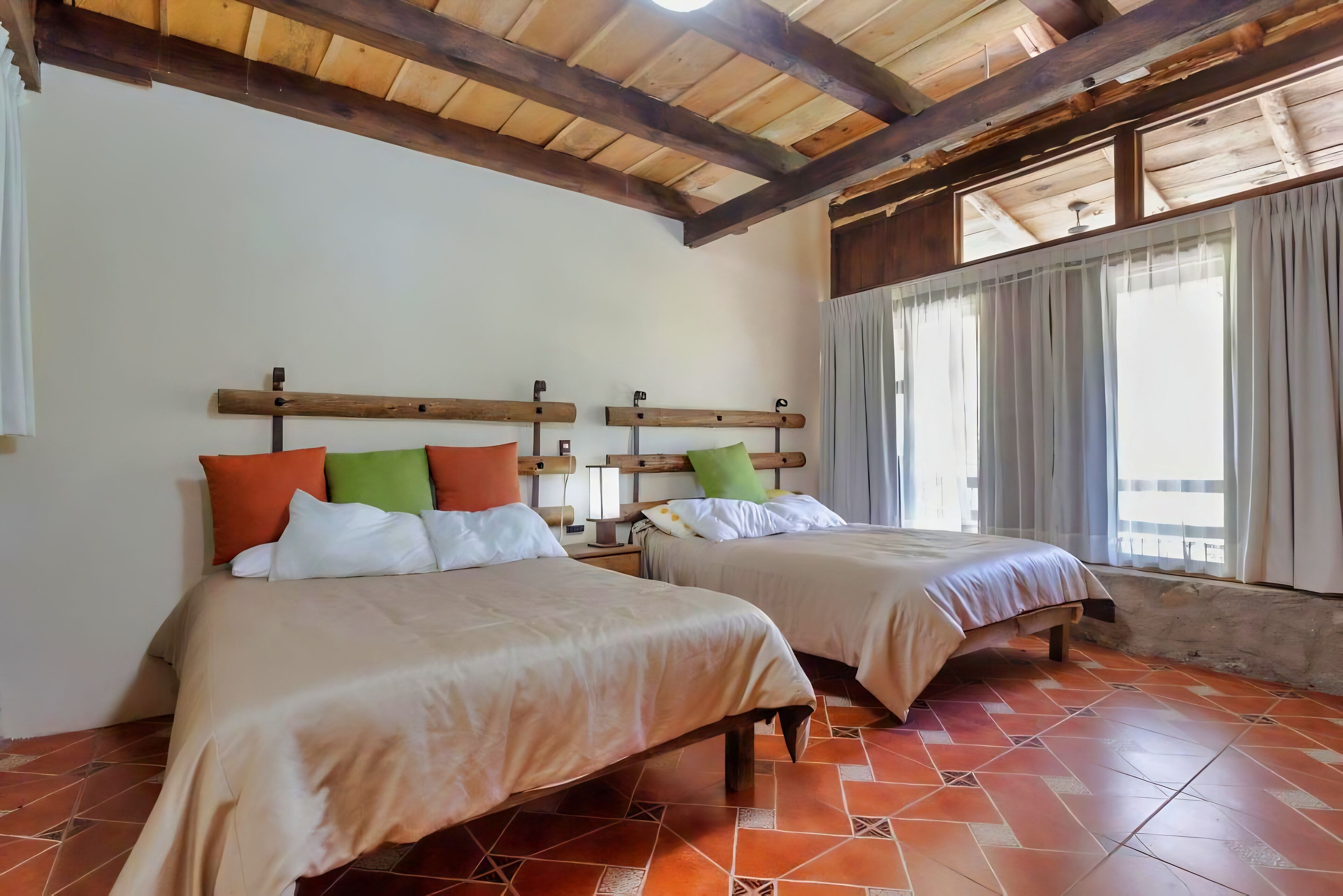 A room with two beds, wooden headboards, a tiled floor, and a window with curtains.