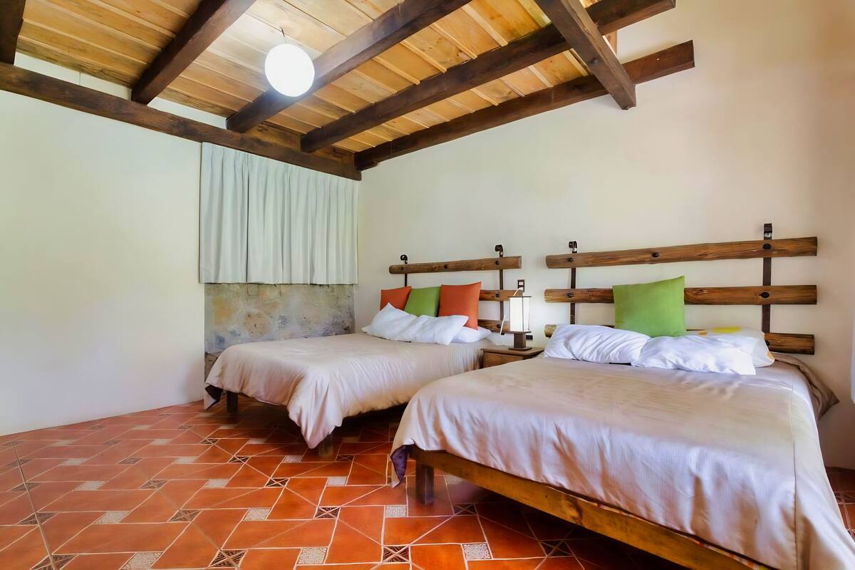 A room with two beds, wooden headboards, a tiled floor, and a ceiling fan.