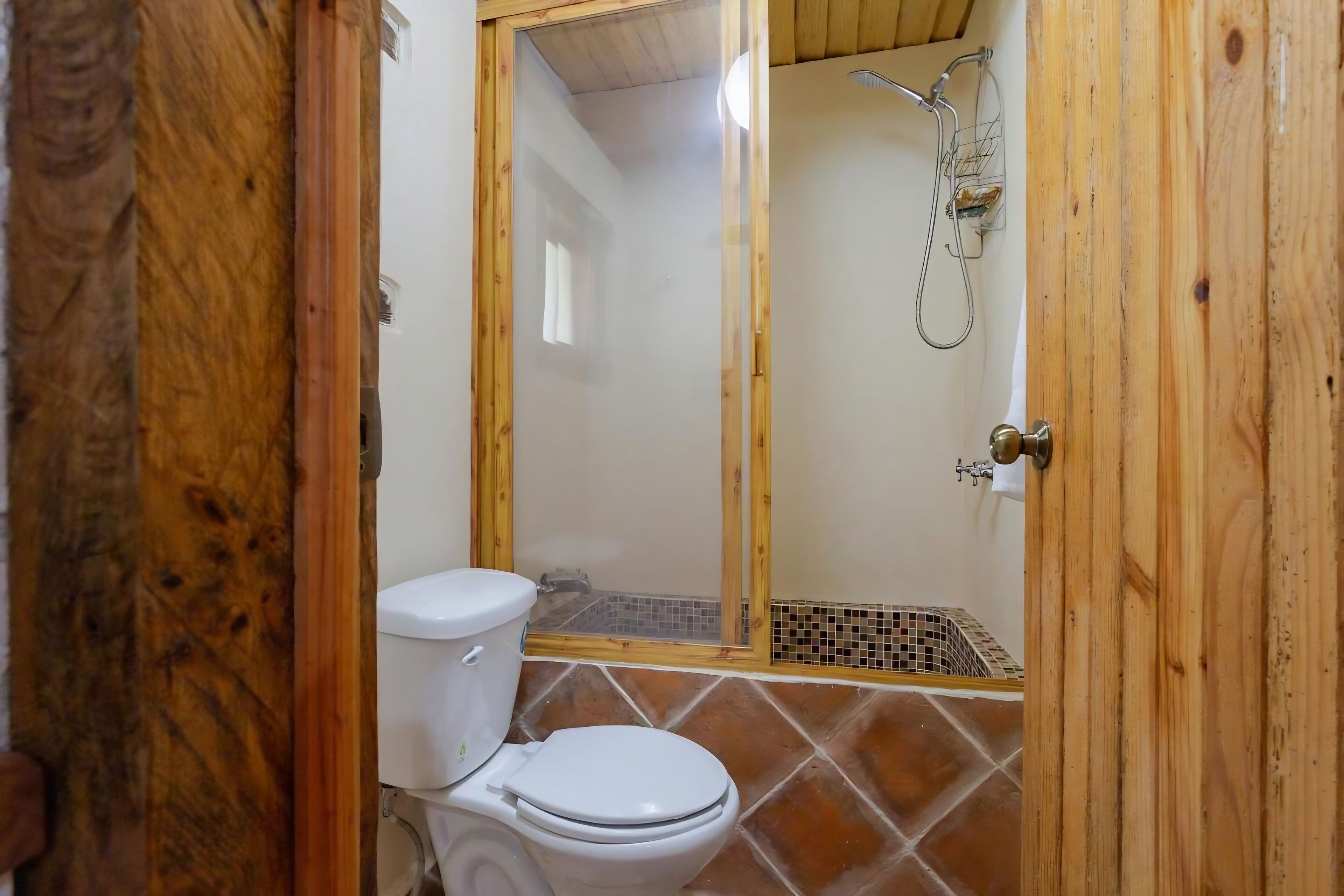 A wooden-framed bathroom with a white toilet, a shower area, and a tiled floor.
