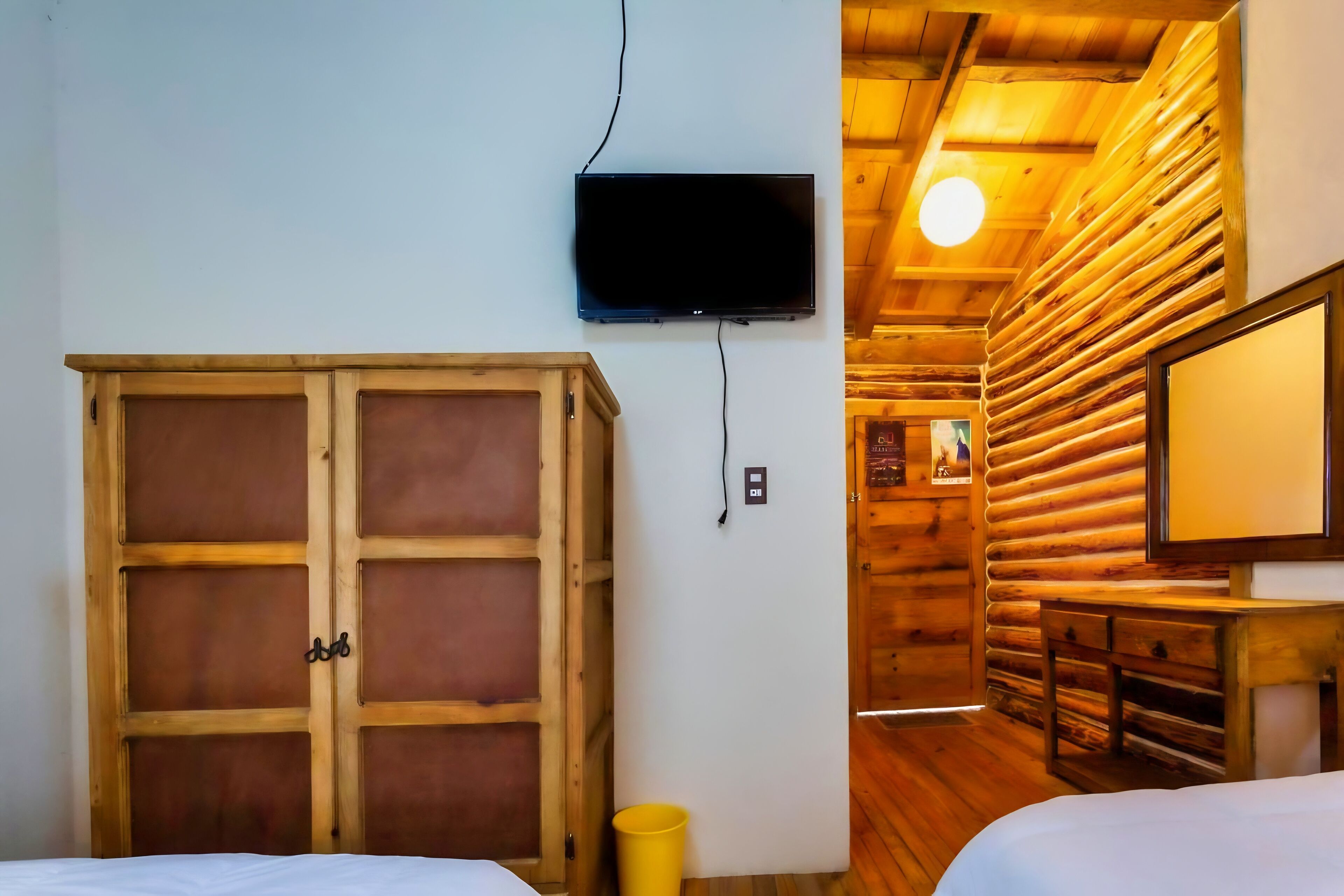 Une chambre de style cabane en bois, avec un téléviseur fixé au mur, une armoire en bois et un lit recouvert d’une couette blanche.