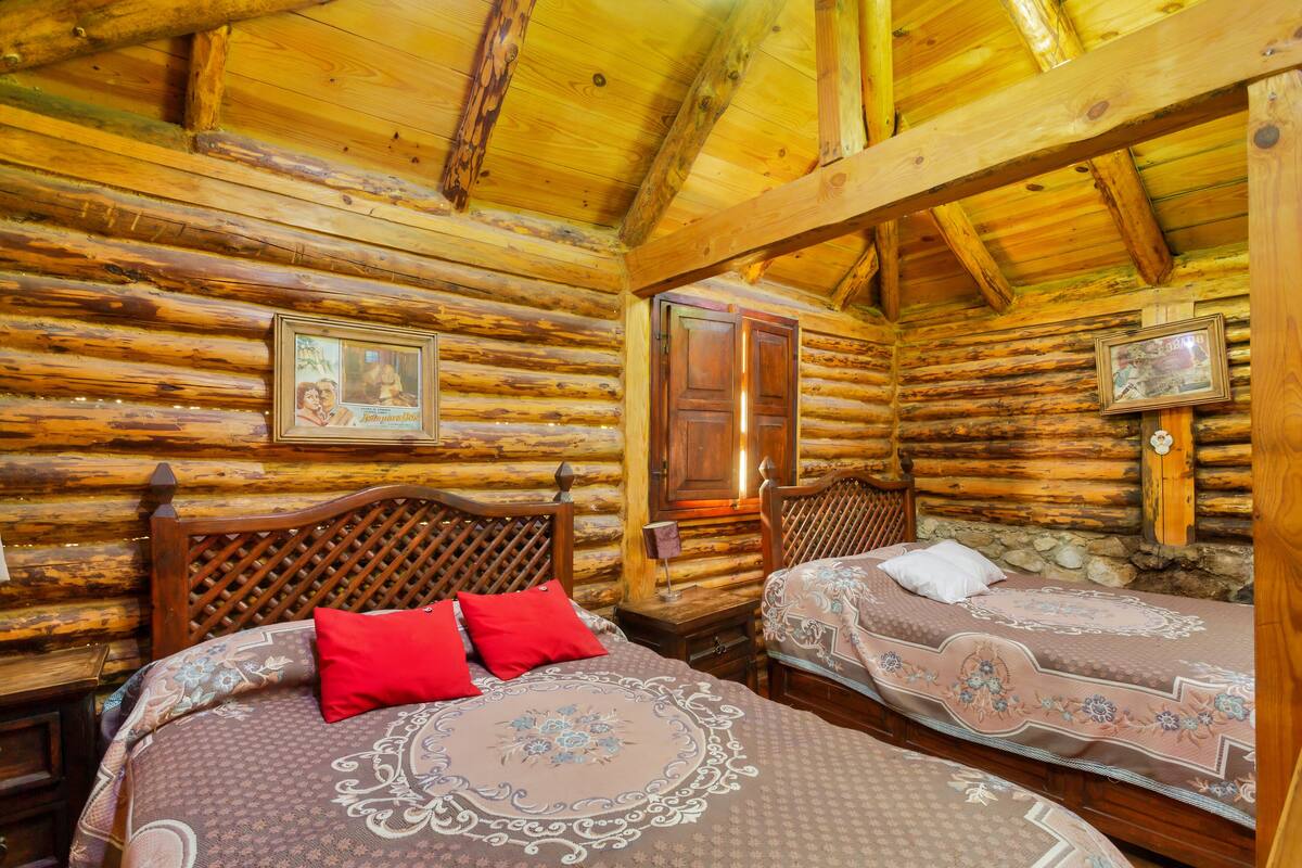 A log cabin room with two wooden beds, a wooden headboard, and a wooden ceiling.