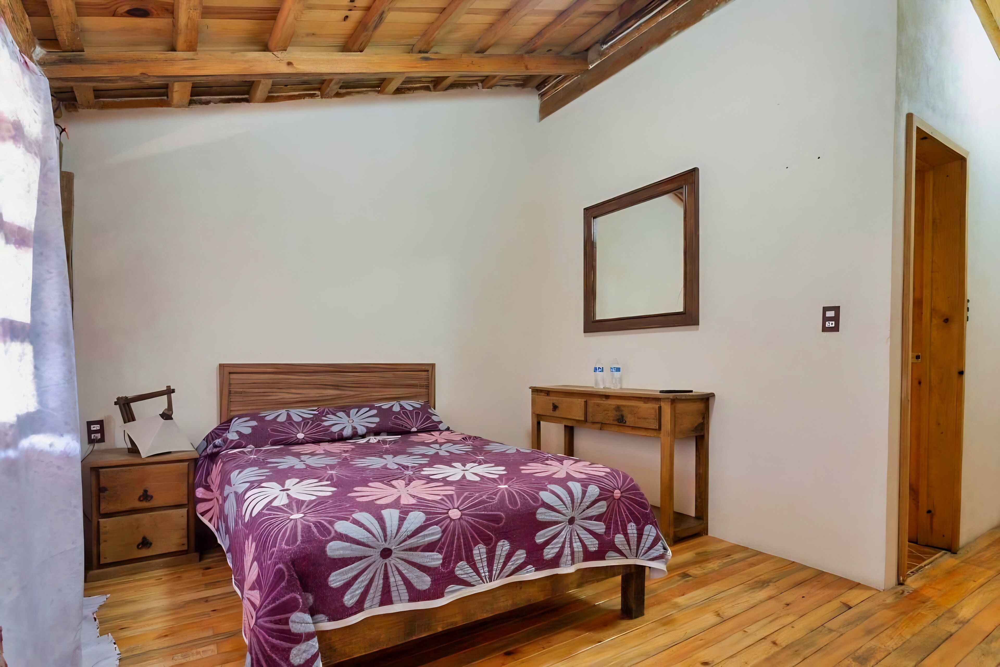 A bedroom with a wooden bed, a nightstand, a bedside table, and a mirror on the wall.