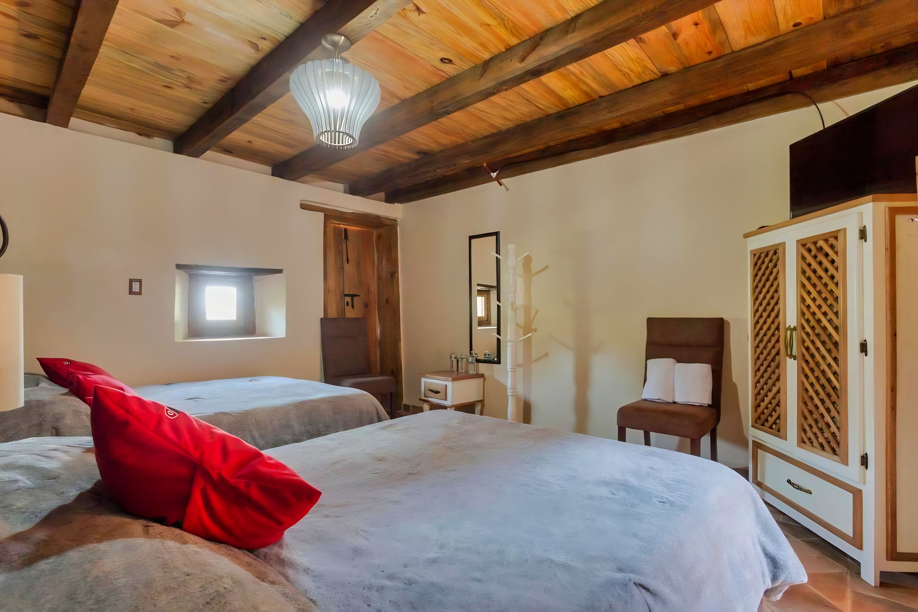 A room with two beds, a wooden ceiling, a wardrobe, and a small window.