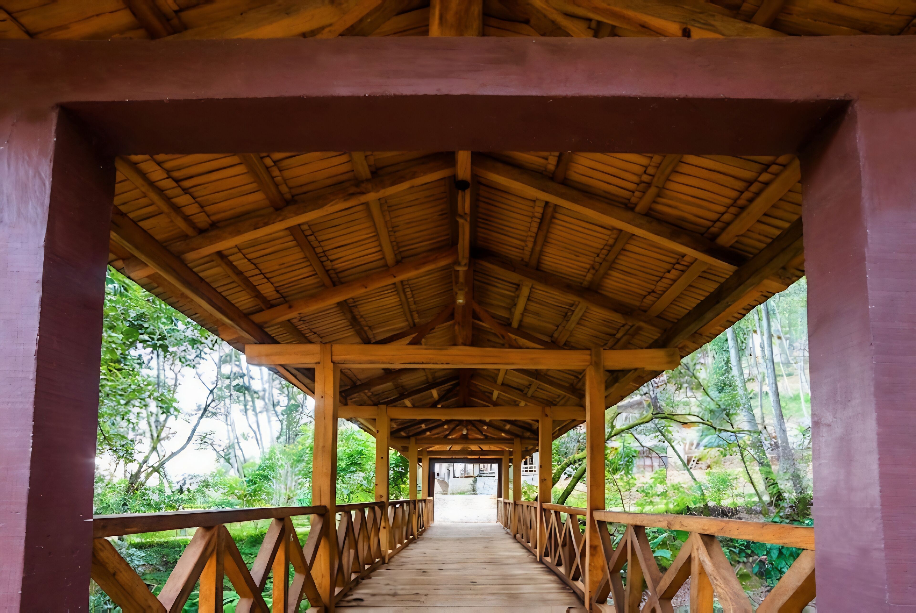 A covered wooden walkway with a thatched roof, surrounded by greenery.