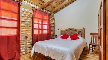 Un dormitorio estilo cabaña de madera con una cama, cortinas rojas y una silla de madera.