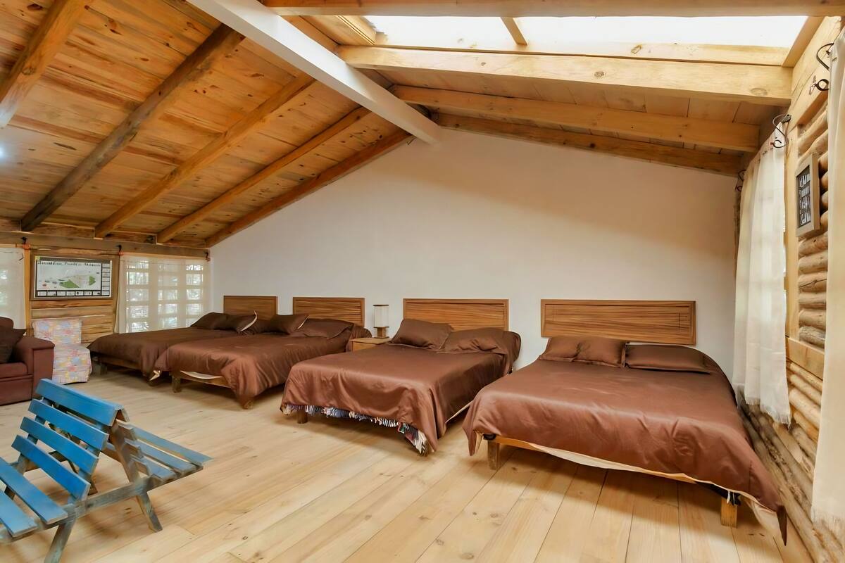 A log cabin-style room with three wooden beds, a blue bench, and a wooden ceiling.
