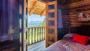 Een houten kamer met balkon, een bed met een bedovertrek met patroon, en een ingelijste foto aan de muur.