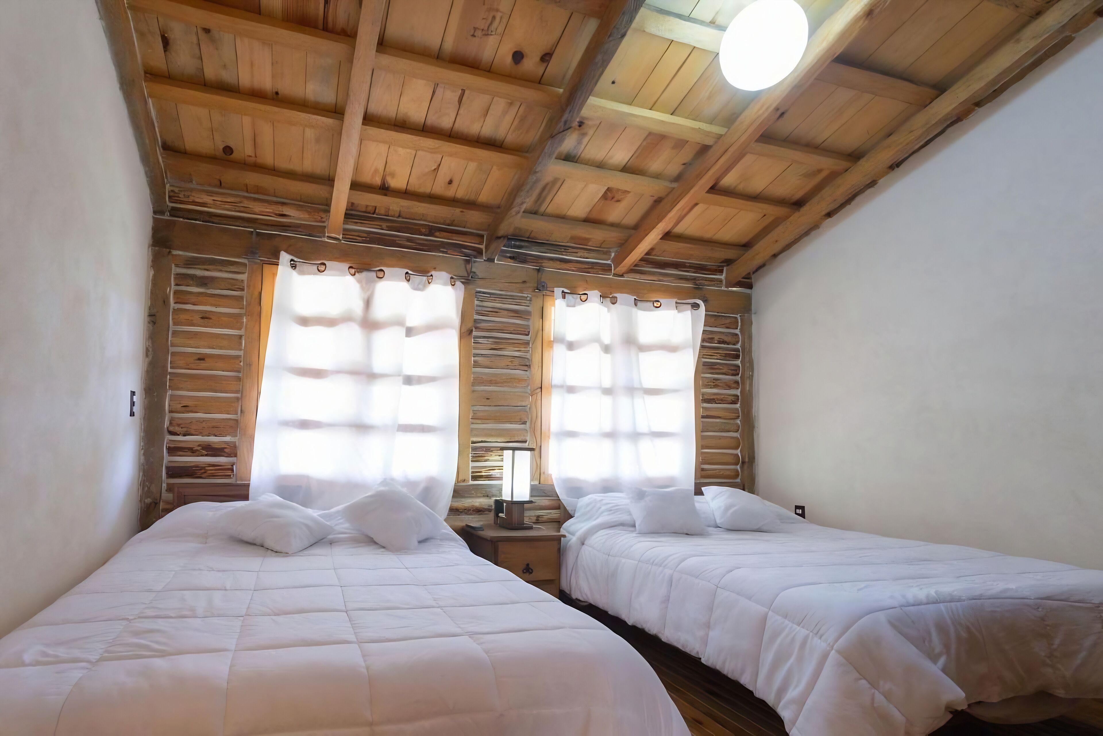 A room with two beds, wooden ceiling beams, and a window with curtains.