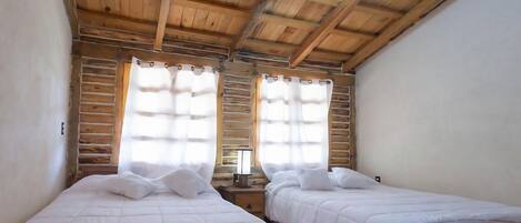 A room with two beds, wooden ceiling beams, and a window with curtains.