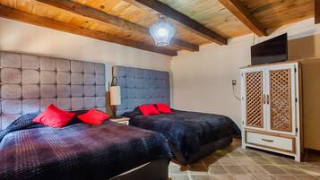 Un dormitorio con dos camas, techo de madera, televisor sobre un mueble bajo y una mesita de noche con lámpara.
