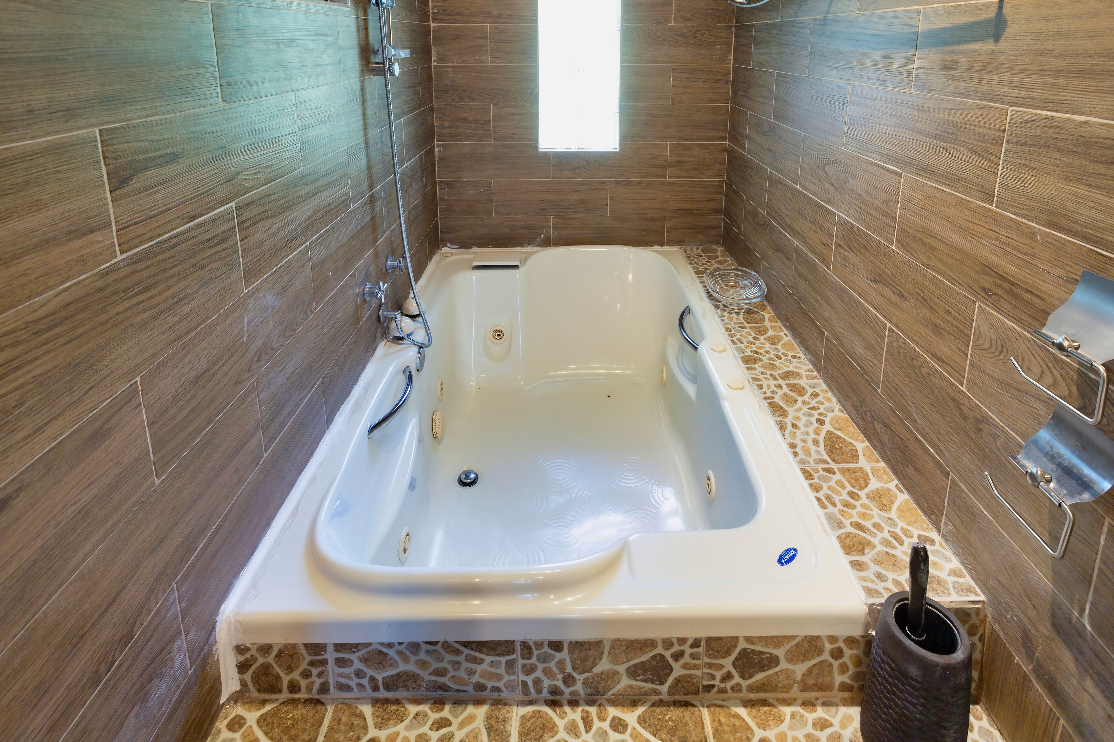 Un baño con una bañera grande, paredes de azulejos y una ventana pequeña.