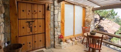 A rustic stone building with a wooden door, a covered patio with a table and chairs, and potted plants.