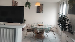 En spiseplads med et rundt bord, fire stole, et fjernsyn og hængende planter.
