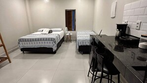 Quarto de hotel compacto com duas camas, um kitchenette pequeno e uma área de jantar.