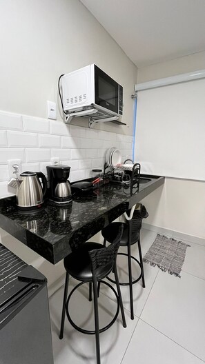 Una cocina compacta equipada con microondas, cafetera, hervidor y dos taburetes de bar.