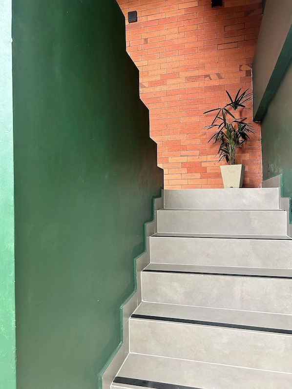 A staircase with a green wall on one side and a brick wall on the other, leading to a landing where a potted plant is placed. - Morada do Sol Suítes - Suíte 04 (Arraial do Cabo)