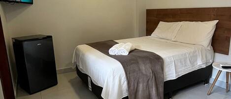A hotel room with a bed, a television, a small refrigerator, and a wall-mounted key rack.