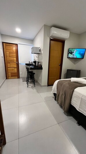 Una habitación de hotel con cama, escritorio con silla, televisor y aire acondicionado.
